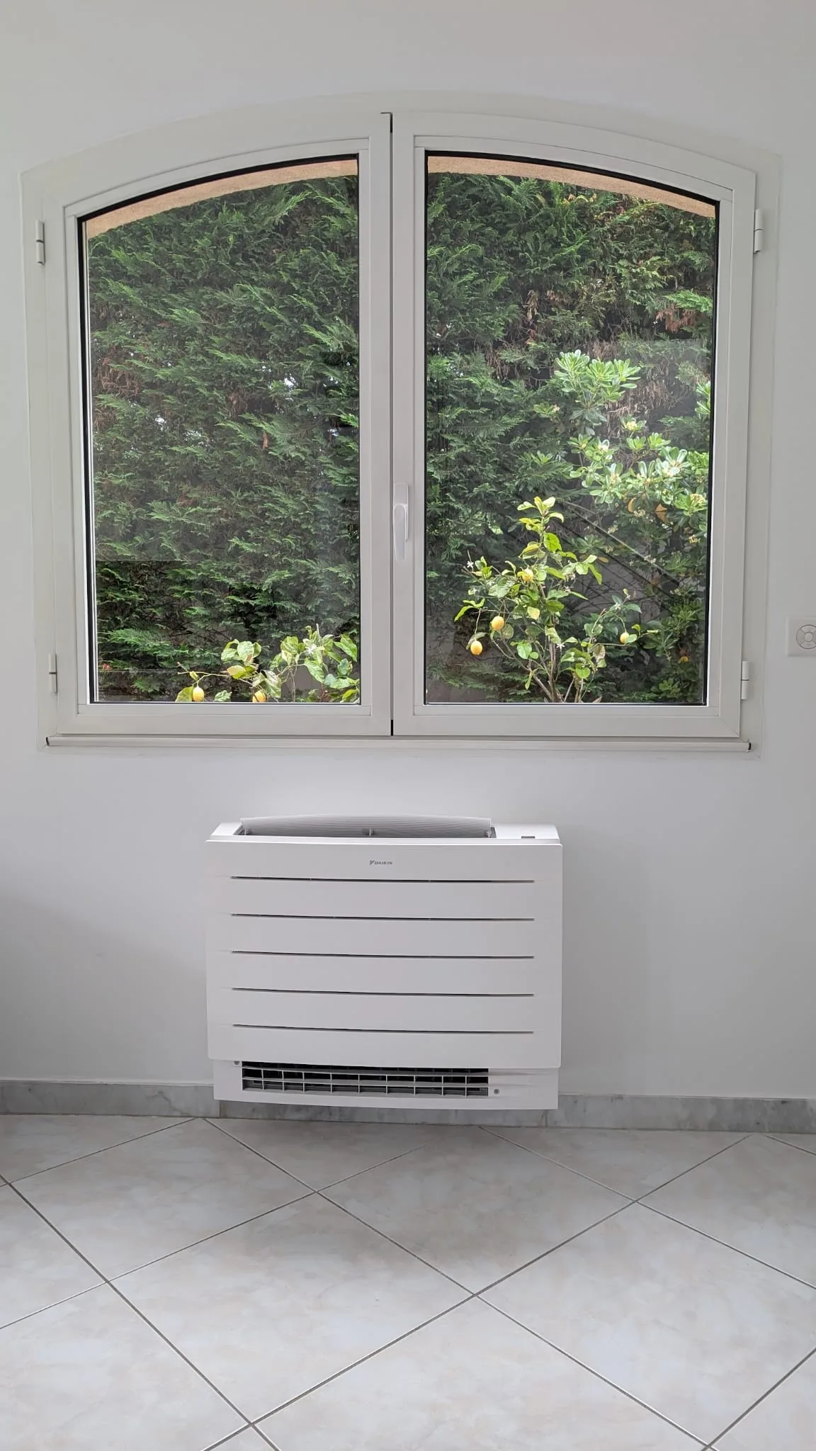 Console de climatisation Daikin intégrée sous une fenêtre cintrée à Marseille, vue sur jardin avec citronnier